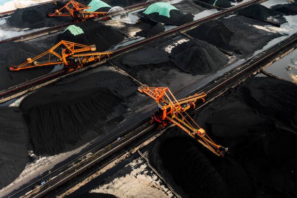 Aerial view of an industrial coal yard with large orange machinery and piles of charcoal.