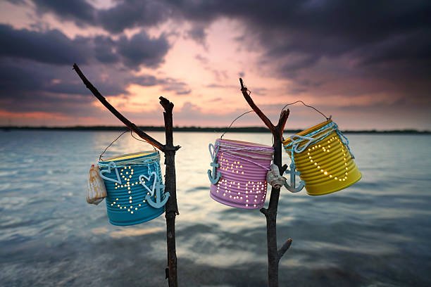 Colorful hanging tin can lanterns glowing by the water at sunset.