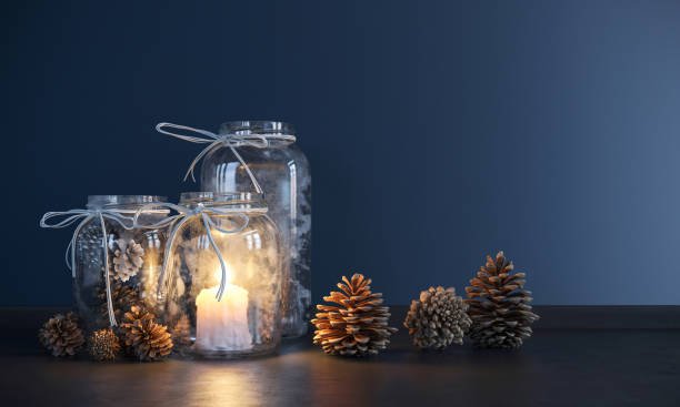 Glowing candle in a glass jar with pinecones against a blue background.